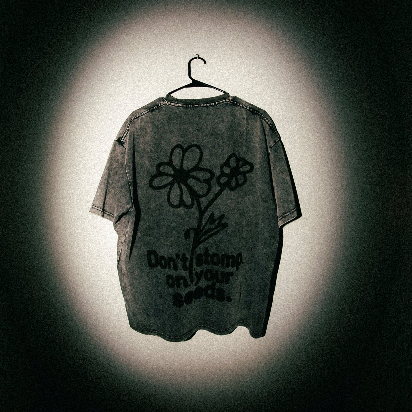 Dark t-shirt with floral design and text on a hanger against a black background
